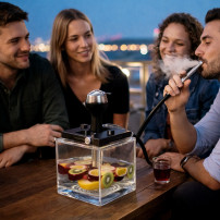 Titanium Cube Wasserpfeife – eine Wasserpfeife mit auf dem Tisch platzierten Früchten, inmitten von Menschen
